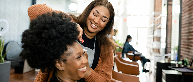 a black female Hairstylist cutting hair for a client in a salon.